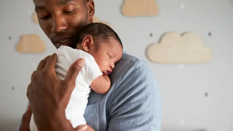 Pai afrodescendente segurando bebê adormecido.