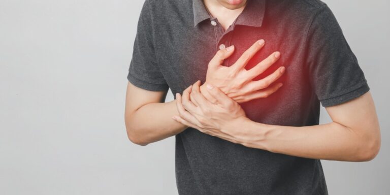 Homem segurando o peito com expressão de dor, indicando possível ataque cardíaco ou dor no coração.