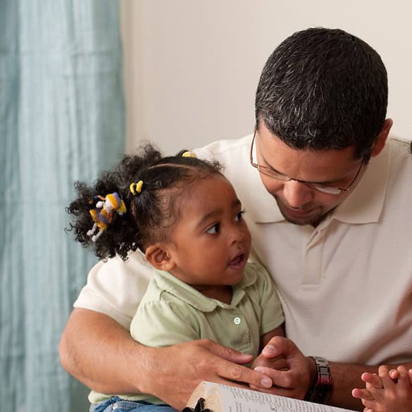 Família unida em momento de oração e leitura, pai, mãe e duas filhas pequenas, em casa, felizes e conectados.