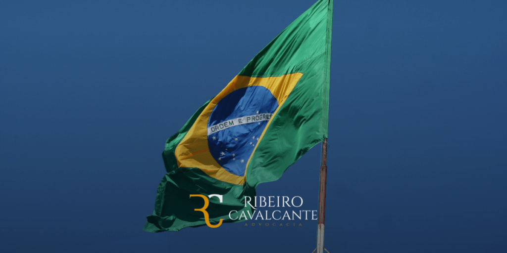 Bandeira do brasil com logotipo do escritório ribeiro cavalcante advocacia ao fundo de céu azul.