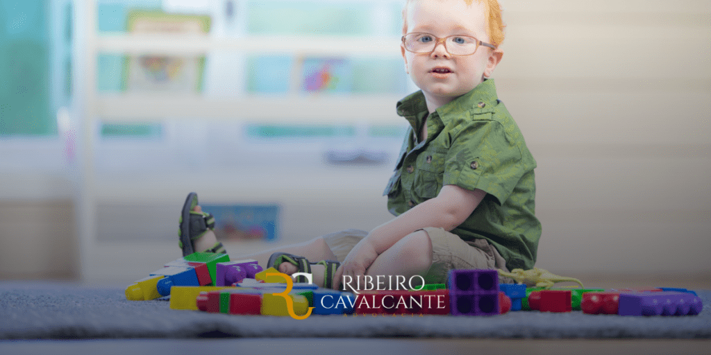 Criança loira com óculos brincando com blocos de montar coloridos em uma sala iluminada. Logotipo ribeiro cavalcante.