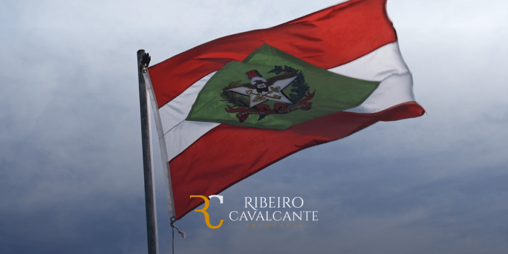 Bandeira do estado de santa catarina tremulando ao vento com céu ao fundo, logotipo ribeiro cavalcante advocacia em destaque.