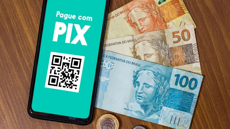 Celular exibe QR Code do PIX junto a notas de Real.